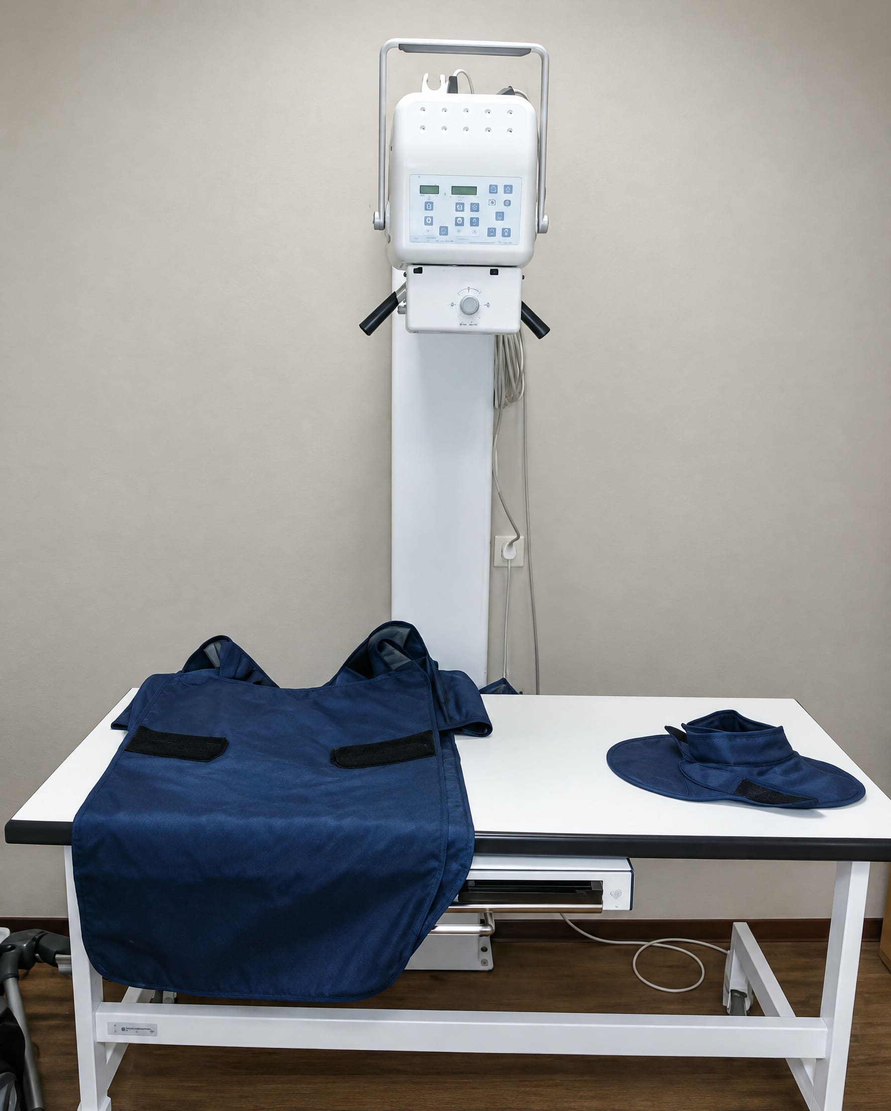 Het röntgentoestel boven een witte tafel, met een donkerblauw loodschort en een schildklierkraag erop.