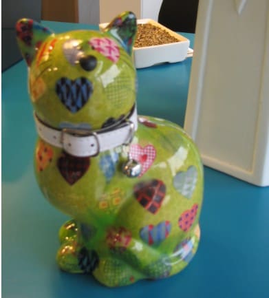 Een vrolijk beschilderd keramisch kattenbeeldje met een halsbandje, op de balie.