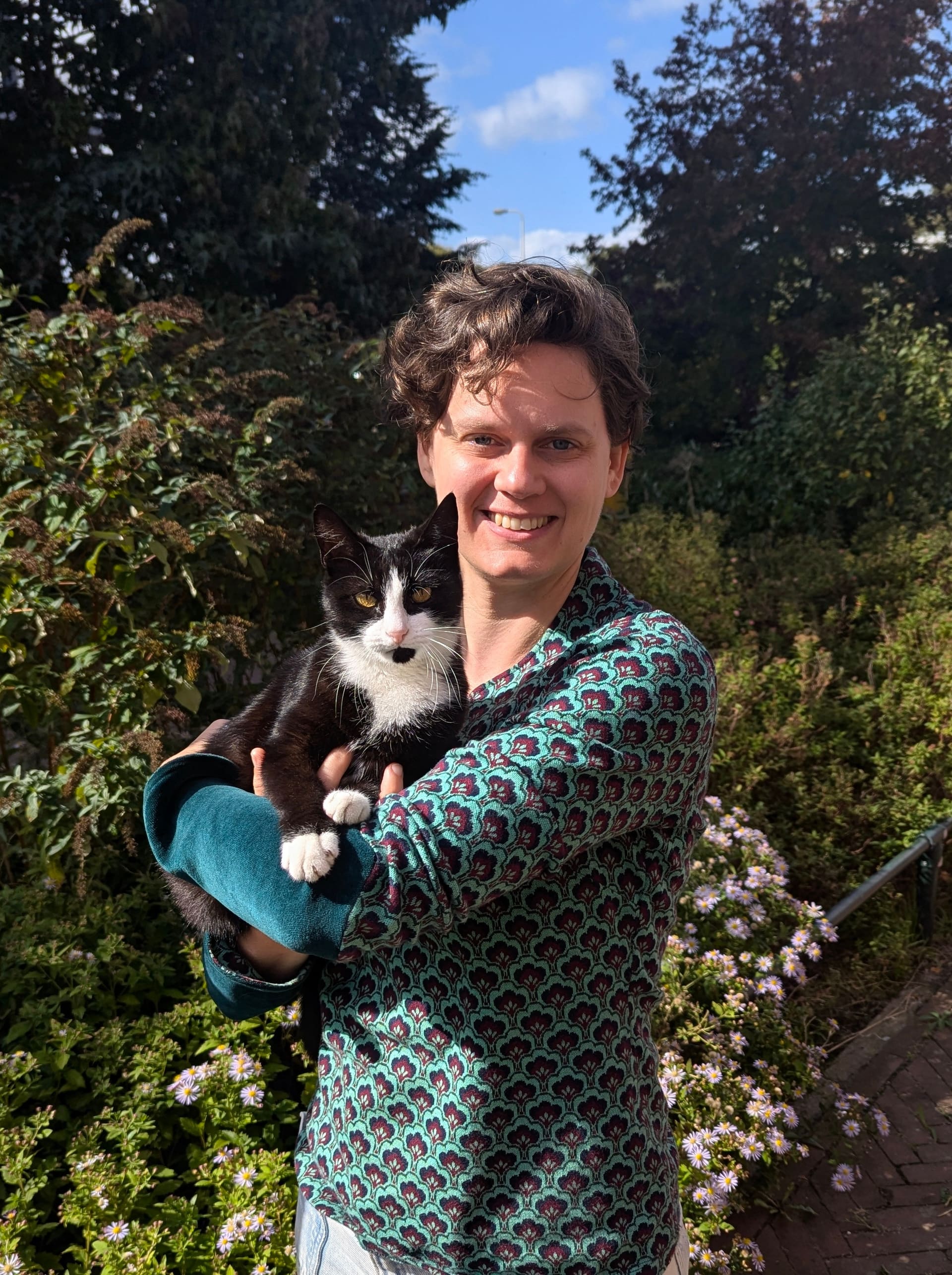 Een zwart-witte kat op de arm in een bloeiende tuin op een zonnige dag.