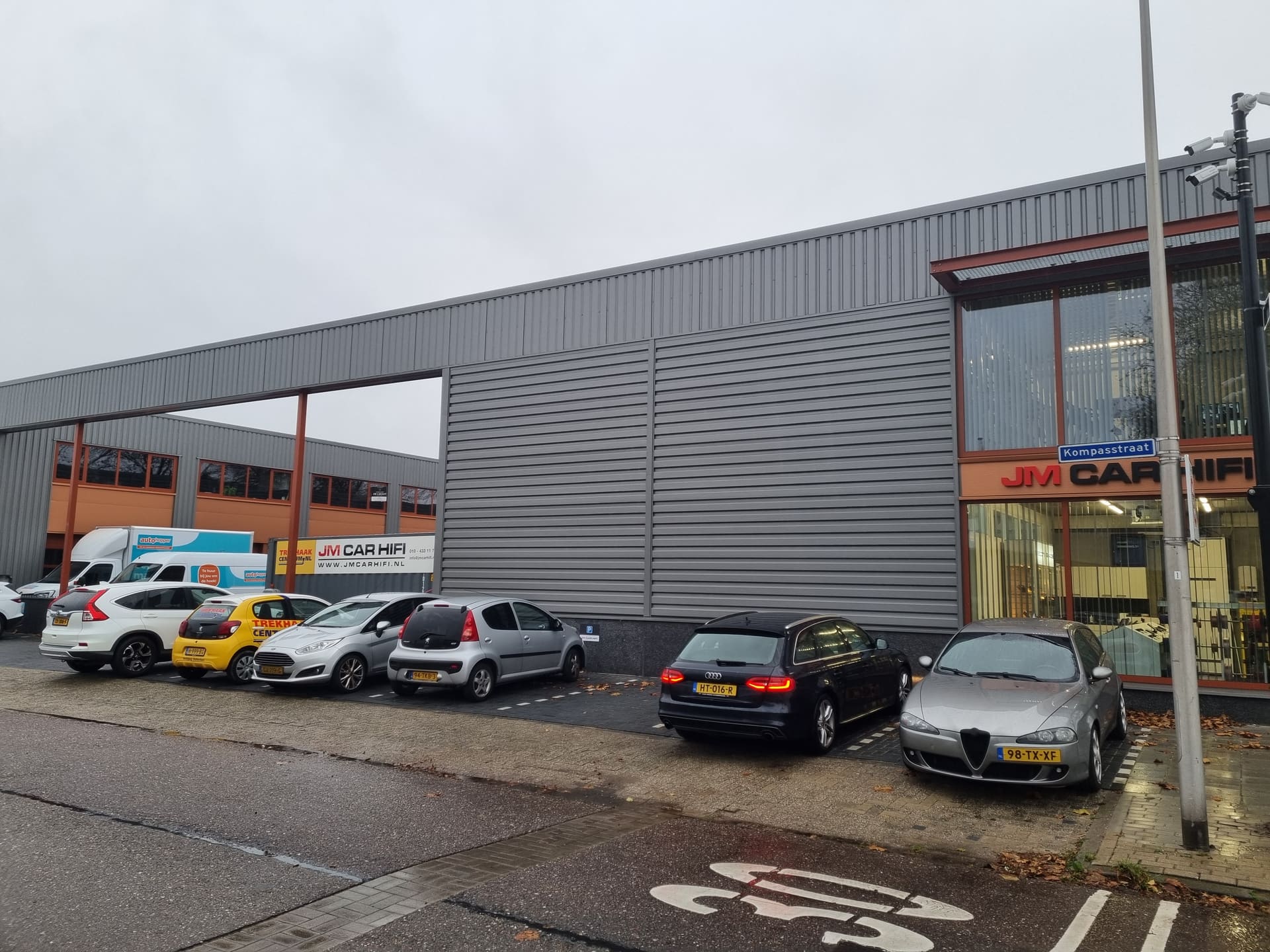 De parkeerplaats aan de Kompasstraat met geparkeerde auto's langs het bedrijfspand.